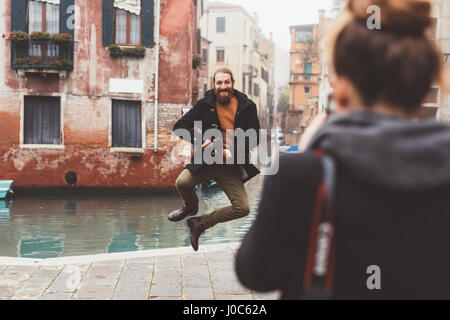 Woman photographing man jumping by canal, Venice, Italy Stock Photo