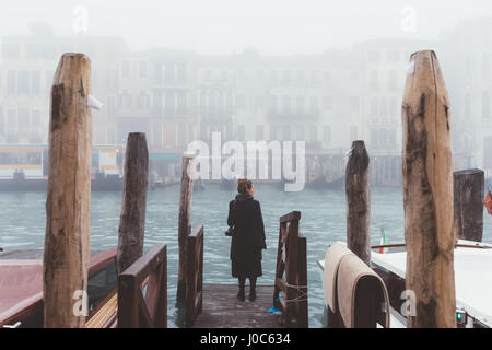 Rear view of woman looking out from misty canal pier, Venice, Italy Stock Photo