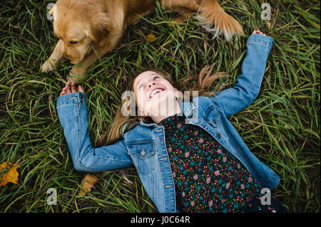 Young girl lying on grass looking up at her Golden Retriever Stock Photo