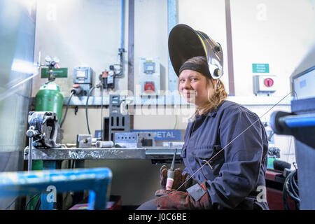 Female apprentice welder holding equipment in car factory, portrait