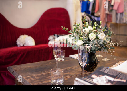 a bouquet of white roses in the interior on the table with glasses of champagne on a background of red sofa Stock Photo