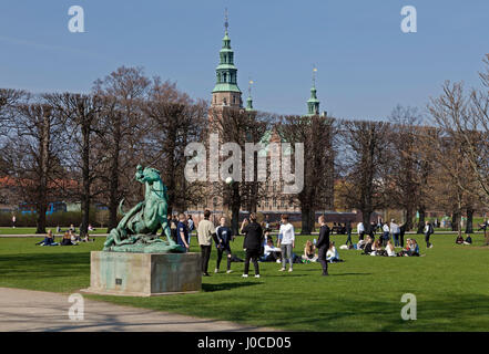 Young people enjoy the warm spring sun on Palm Sunday in Kongens Have, the King's garden, Copenhagen, Denmark. The Rosenborg Castle in the background. Stock Photo