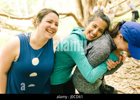 Three adult sisters hugging and laughing in forest, Maine, USA Stock Photo