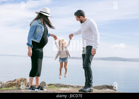 Pregnant mature couple swinging daughter at coast Stock Photo