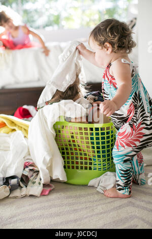 Female toddler removing laundry from child hiding in laundry basket Stock Photo