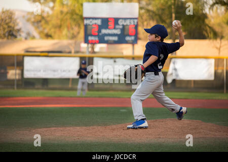 Boy baseball pitcher throwing ball on baseball field Stock Photo