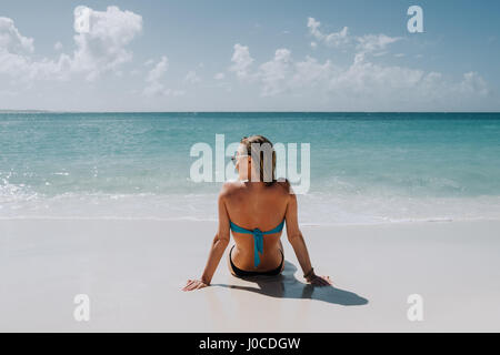 Rear view of woman in bikini sitting on beach looking out at blue sea, Anguilla, Saint Martin, Caribbean Stock Photo