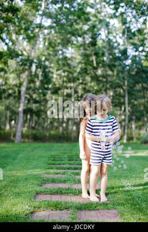Girl and boy watching bubbles from toy bubble maker in garden Stock Photo