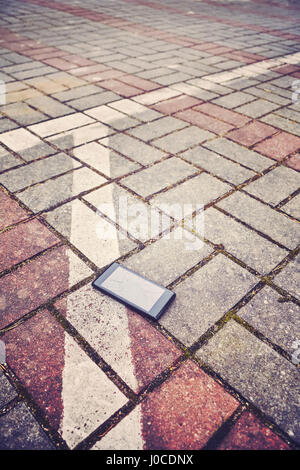 Vintage stylized picture of a mobile phone with broken screen on a parking pavement, selective focus. Stock Photo