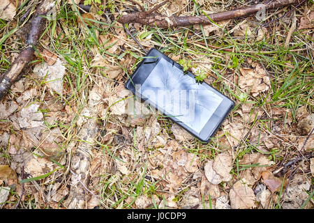 Close up picture of a mobile phone with broken screen on a ground in a park. Stock Photo