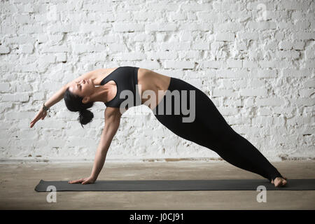 Young yogi attractive woman in Vasisthasana pose, white loft bac Stock Photo