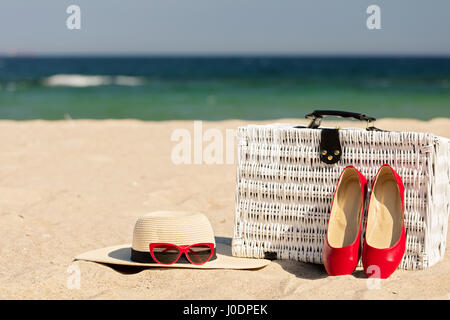 Summer vacation at sea. White wicker suitcase and women's accessories and shoes on the beach. Selective focus. Stock Photo