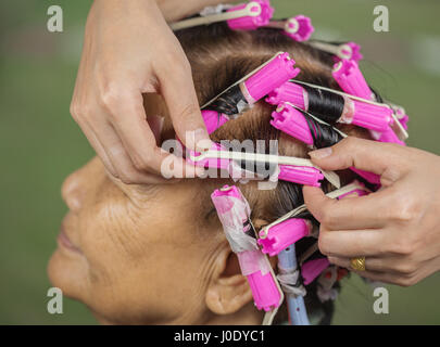 hand of a hairstylist doing a perm rolling the hair of senior woman Stock Photo