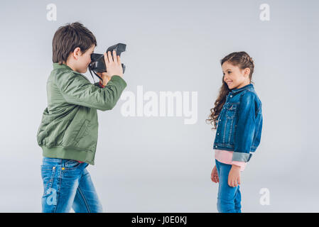 Boy taking pictures of girl on retro camera on gray Stock Photo