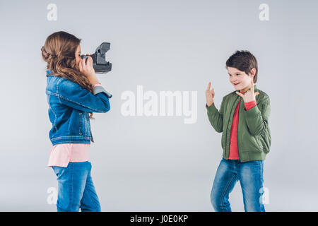 Girl taking pictures of boy on retro camera on gray Stock Photo