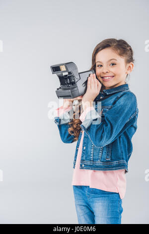 Adorable girl taking pictures on retro camera on gray Stock Photo