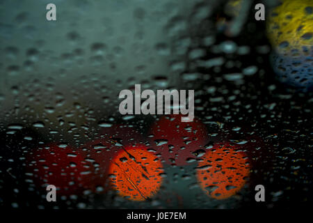 Night view of the city lights through the window in the rain, rain drops falling on the windshield of the car. Abstract light bokeh, defocused background Stock Photo