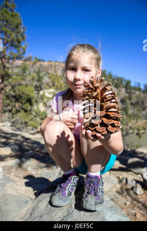 Young girl holding giant pinecone in hand. Hiking path in Teno mountains, Tenerife, Canary, Spain Stock Photo