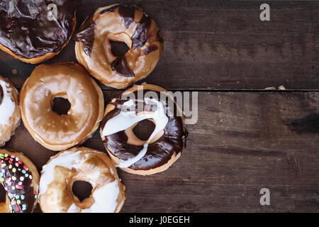 Background of chocolate, carmel, glazed and filled donuts over a rustic background with copy space. Image shot from overhead. Stock Photo