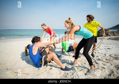 Friends helping man and woman while playing tug of war at beach Stock Photo