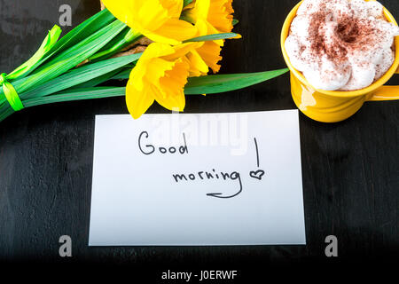 Coffee mug with yellow daffodil flowers and quotes good morning on white rustic table. Mothers day or Womens day. Greeting card. Top view. Breakfast Stock Photo