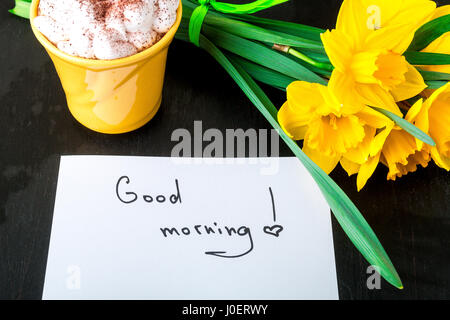 Coffee mug with yellow daffodil flowers and quotes good morning on white rustic table. Mothers day or Womens day. Greeting card. Top view. Breakfast Stock Photo