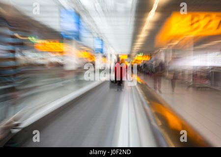Rushing through the airport terminal to catch the next layover flight. Motion blurry image on an escalator. Last minute hurry to not to be late to the Stock Photo