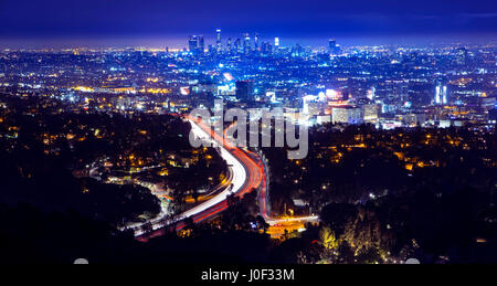 Los Angeles city skyline and highway 101 viewed from West Hollywood hills or heights. Trails of light from cars and traffic. Stock Photo