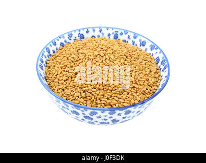 Fenugreek seeds in a blue and white porcelain bowl with a floral design, isolated on a white background Stock Photo