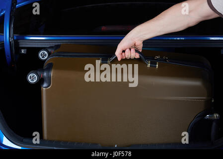 Hand take luggage from car trunk close-up. Taking suitcase from vehicle back Stock Photo