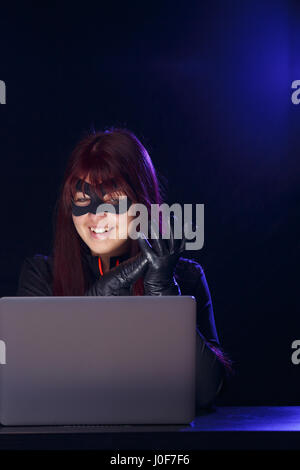 Brunette thief in black mask hacking computer Stock Photo