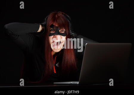 Brunette hacker in black mask screaming at computer Stock Photo