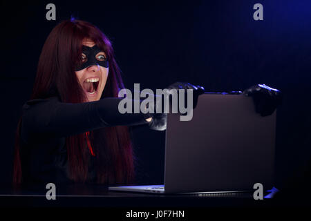 Thief in black mask at night near computer Stock Photo