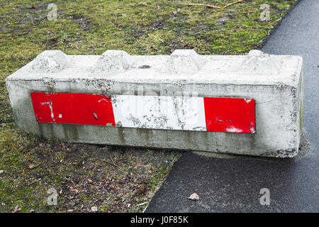 Concrete road block with red white striped warning sign lays on the roadside Stock Photo