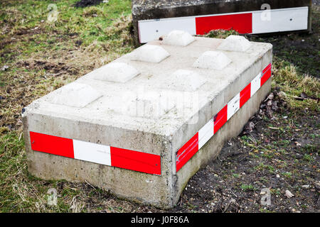 Concrete road blocks with red white striped warning signs lay on green grass Stock Photo