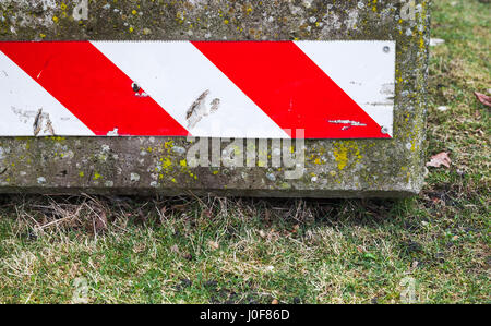 Concrete road block with red white striped warning sign lays on green grass Stock Photo