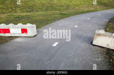 Concrete road blocks with red white striped warning sign lay on the roadsides Stock Photo