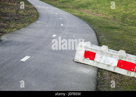 Concrete road block with red white striped warning sign lays on the roadside Stock Photo