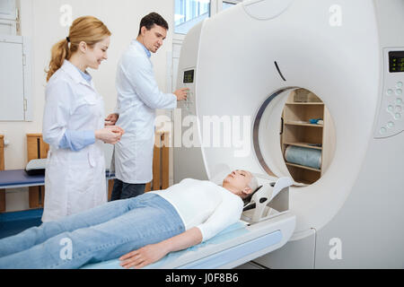 Do not worry. Handsome experienced male doctor looking at his patient and pressing the button while using CT scanner Stock Photo