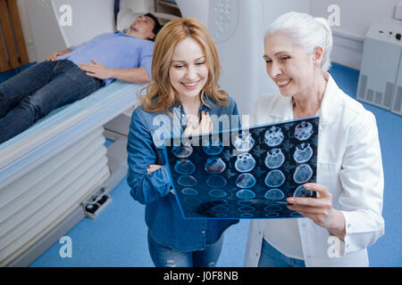 No serious problems. Cheerful delighted positive woman standing near the oncologist and talking to her while looking at the X ray photo Stock Photo