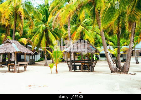 Nipa huts on the white coral sand beach surounded with palms Stock Photo