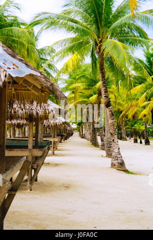 Nipa huts on the white coral sand beach surounded with palms Stock Photo