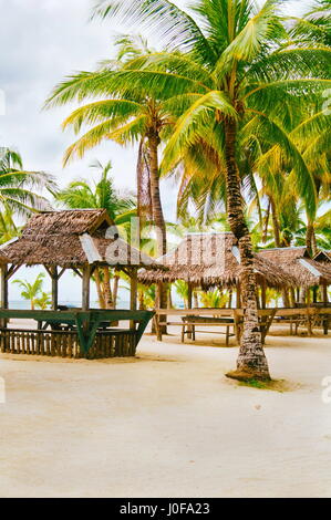 Nipa huts on the white coral sand beach surounded with palms Stock Photo