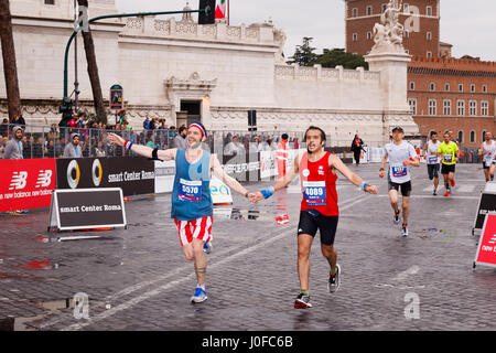 Rome, Italy - April 2nd, 2017: Athletes participating in the 23rd Rome Marathon exhausted reach, hand in hand, the line in Via dei Fori Imperiali. Stock Photo