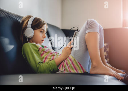 Girl sitting on black sofa using tablet and listening music
