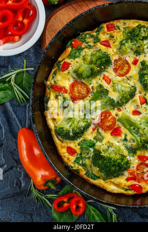 Frittata with broccoli, spinach, sweet peppers and tomatoes in iron skillet. Kind of Italian omelette with vegetables. Top view Stock Photo