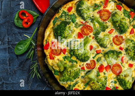 Frittata with broccoli, spinach, sweet peppers and tomatoes in iron skillet. Kind of Italian omelette with vegetables. Stock Photo