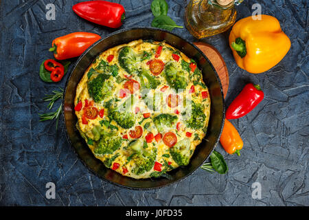 Frittata with broccoli, spinach, sweet peppers and tomatoes in iron skillet. Kind of Italian omelette with vegetables. Top view Stock Photo