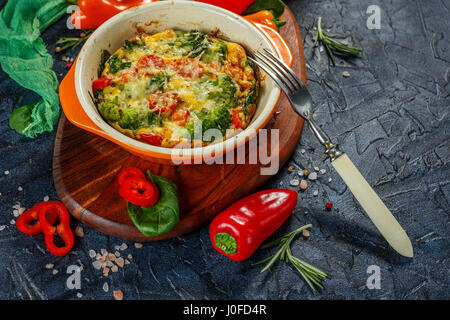 Frittata with broccoli, spinach, sweet peppers and tomatoes in ceramic baking dish. Italian omelet with vegetables. Stock Photo