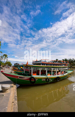 Vertical riverscape with traditional wooden long boats on the Thu Bon river in Hoi An, Vietnam. Stock Photo